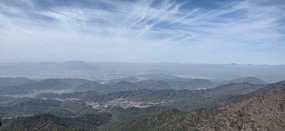 푸른 하늘 아래 겹겹이 쌓인 산맥과 멀리 보이는 도시의 전경이 펼쳐진 풍경입니다.