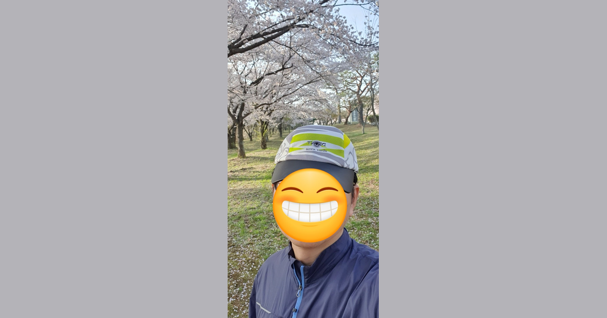 벚꽃이 만개한 공원을 배경으로 모자와 파란색 상의를 입은 사람이 서 있습니다.