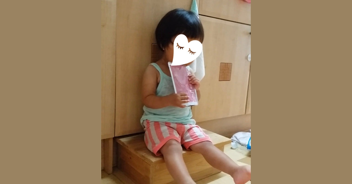 어린아이가 나무 발판에 걸터앉아 양손으로 한약 파우치를 들고 마시고 있는 모습