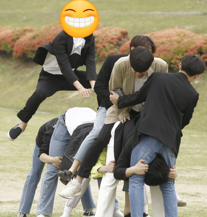 야외 잔디밭에서 여러 명의 남성들이 말뚝박기 놀이를 하며 즐거운 시간을 보내고 있습니다.